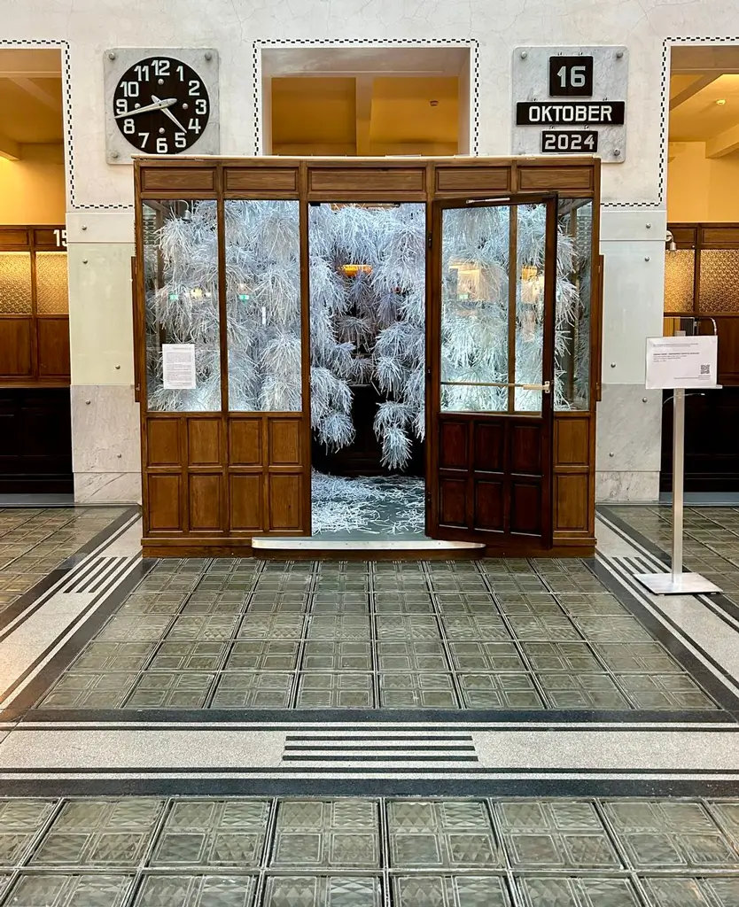 Installation view of &ldquo;Sensing Theory &ndash; Shredding Cognitive Overload.&rdquo; A wooden-panelled cabin with windows in which dense bundles of shredded white paper hang from the ceiling. Loose paper strips cover the floor. The installation is situated inside a large hall.