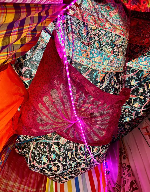 Installation view of &ldquo;Hallabudda Reenactment&rdquo;. Ceiling of the space covered with multicoloured patterned fabrics. A purple LED light chain runs diagonally across the centre.