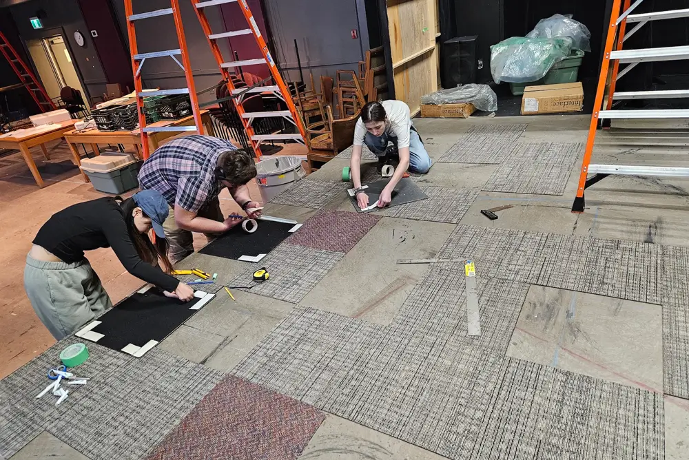 An image of three young people installing carpet tile in a theatre.