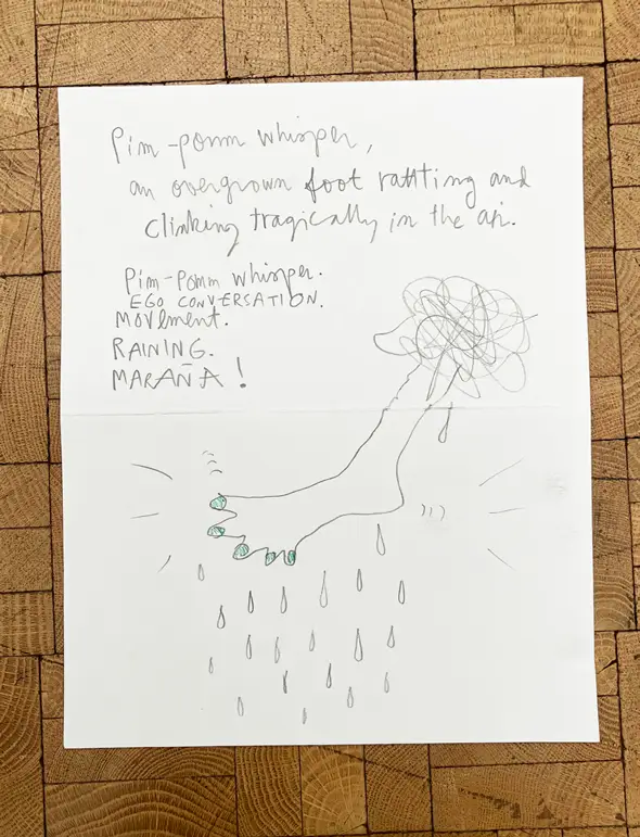 A sheet of paper shows handwritten text and a pencil drawing of a foot with raindrops falling beneath it, placed on a wooden surface.