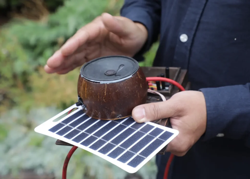 Close-up of the Feedback Coconut in Alejandro Olarte&rsquo;s hands. It is set on top of the Solar Pandora Box.