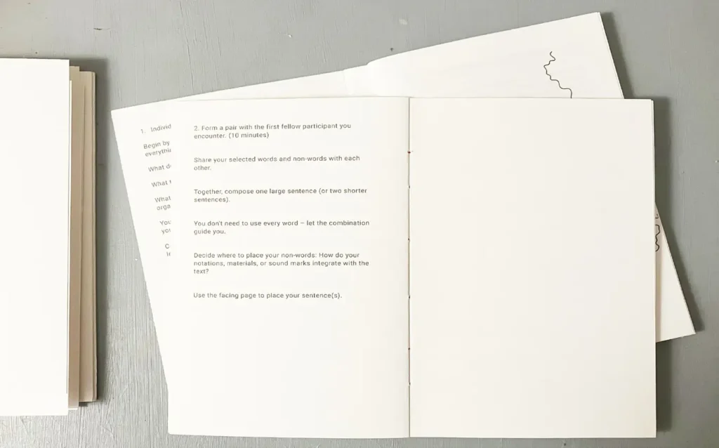 An open workshop booklet lies on a gray surface, showing printed text with instructions for participants to form pairs and compose shared sentences.